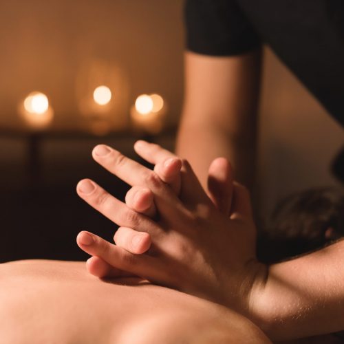 Men’s hands make a therapeutic neck massage for a girl lying on a massage couch in a massage spa with dark lighting. Close-up. Dark Key Men's hands make a therapeutic neck massage for a girl lying on a massage couch in a massage spa with dark lighting. Close-up. Dark Key.